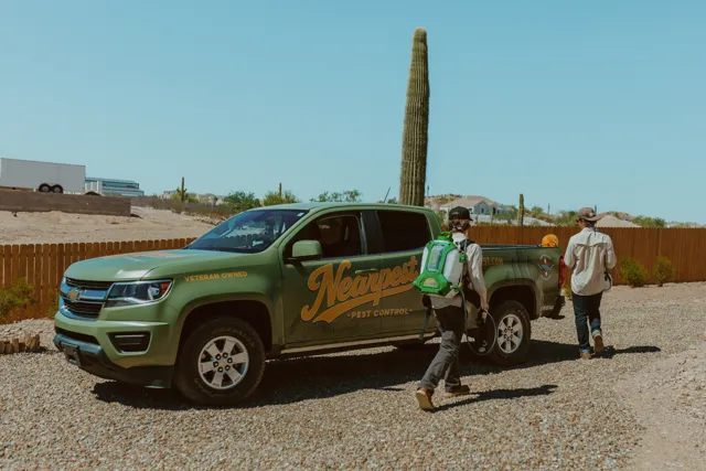 NEARPEST team beside the olive and gold branded pickup in a desert yard