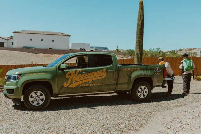 NEARPEST team beside the olive and gold branded pickup in a desert yard