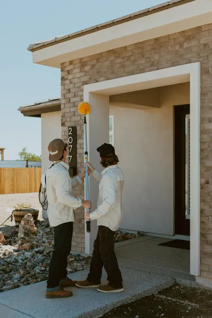 NEARPEST team removing webs around a home entry with a long-handled duster