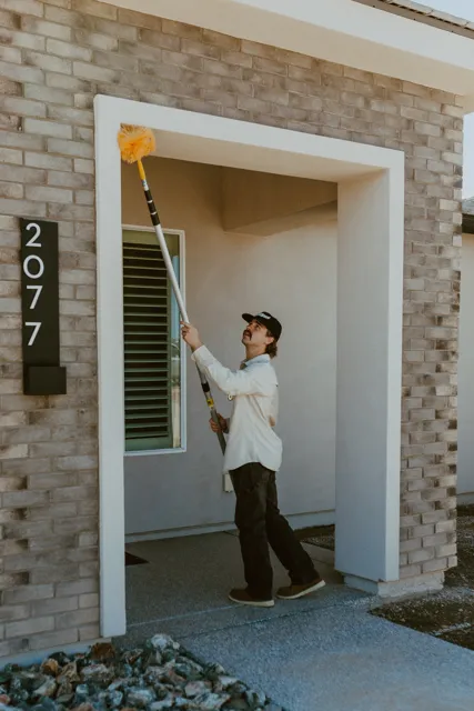 NEARPEST team removing webs around a home entry with a long-handled duster