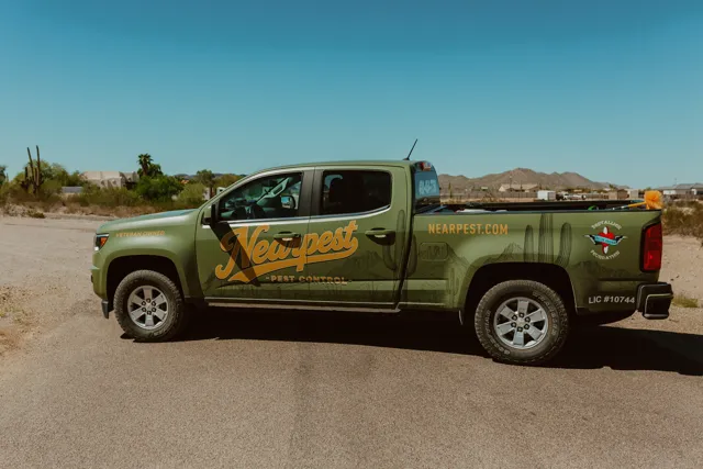 Olive and gold NEARPEST pickup parked beside desert landscaping