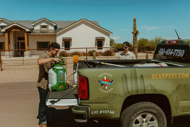 NEARPEST team member preparing a green backpack sprayer beside the pickup