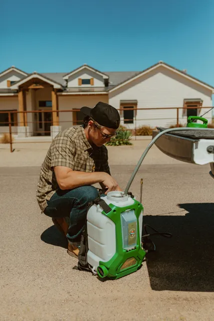 NEARPEST team member preparing a green backpack sprayer beside the pickup