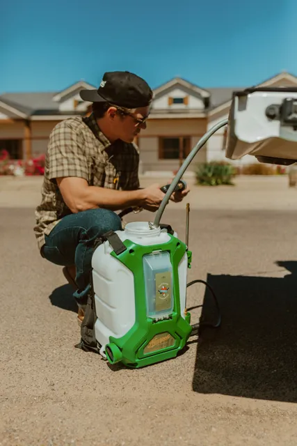 NEARPEST team member preparing a green backpack sprayer beside the pickup