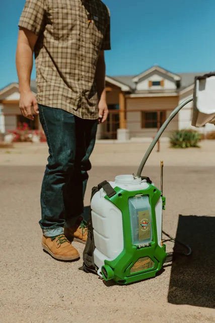 NEARPEST team member preparing a green backpack sprayer beside the pickup
