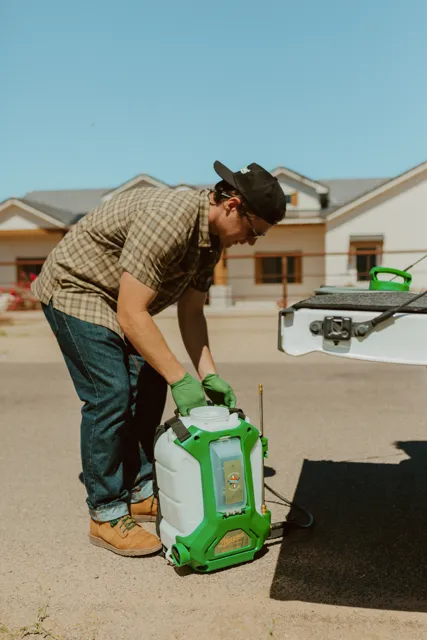 NEARPEST team member preparing a green backpack sprayer beside the pickup