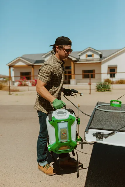 NEARPEST team member lifting and fitting a green backpack sprayer at the tailgate