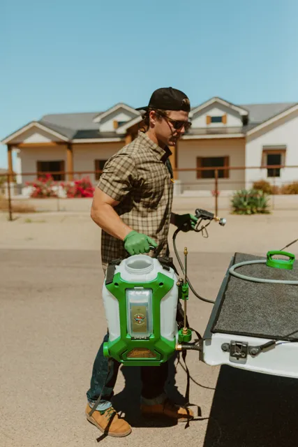 NEARPEST team member lifting and fitting a green backpack sprayer at the tailgate
