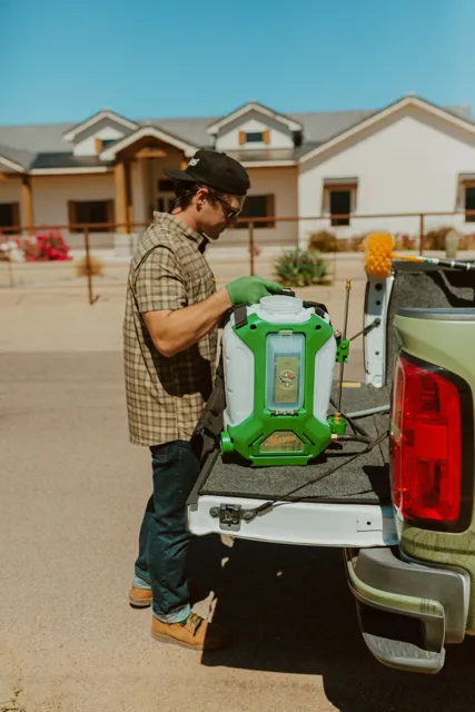 NEARPEST team member lifting and fitting a green backpack sprayer at the tailgate
