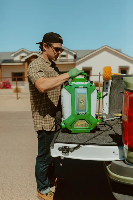 NEARPEST team member lifting and fitting a green backpack sprayer at the tailgate