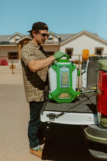 NEARPEST team member lifting and fitting a green backpack sprayer at the tailgate