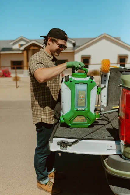 NEARPEST team member lifting and fitting a green backpack sprayer at the tailgate