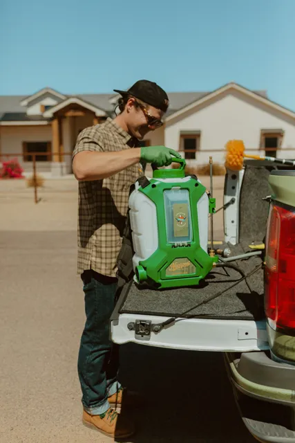 NEARPEST team member lifting and fitting a green backpack sprayer at the tailgate
