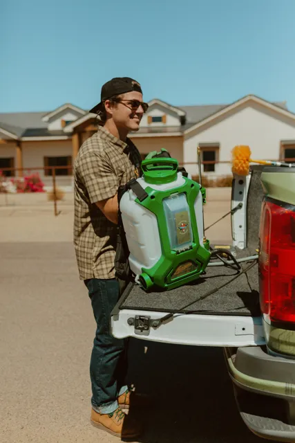 NEARPEST team member lifting and fitting a green backpack sprayer at the tailgate