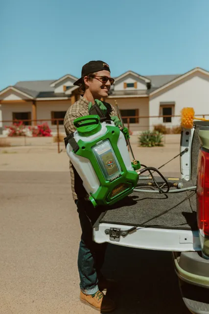 NEARPEST team member lifting and fitting a green backpack sprayer at the tailgate