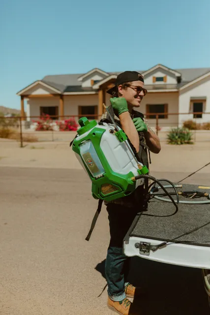 NEARPEST team member lifting and fitting a green backpack sprayer at the tailgate