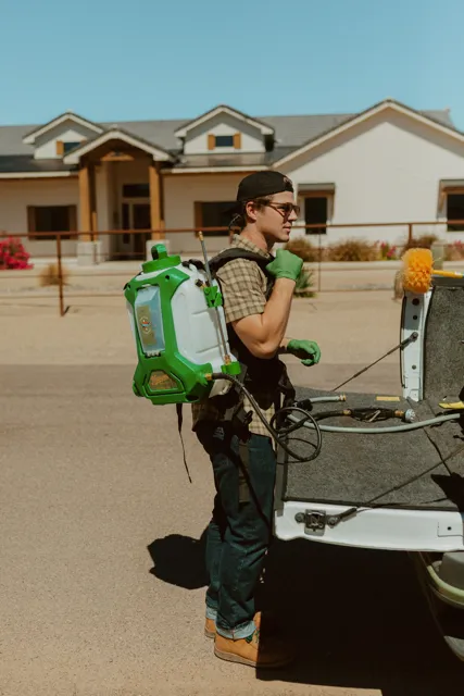NEARPEST team member lifting and fitting a green backpack sprayer at the tailgate