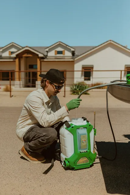 NEARPEST team member in a light shirt preparing a backpack sprayer beside the pickup