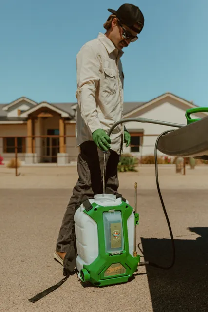 NEARPEST team member in a light shirt preparing a backpack sprayer beside the pickup