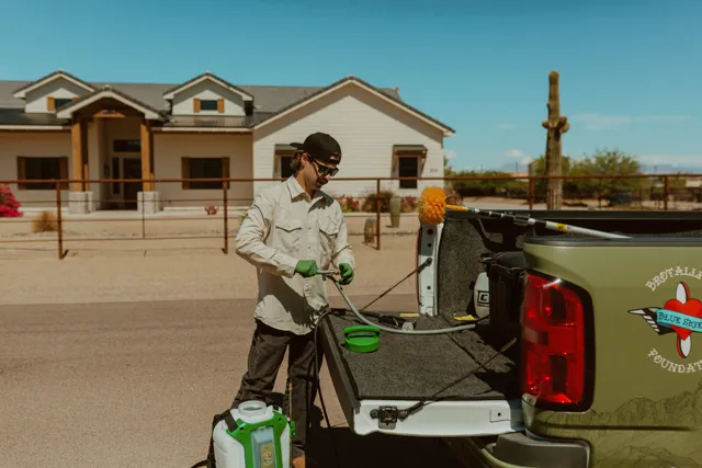 NEARPEST team member in a light shirt preparing a backpack sprayer beside the pickup