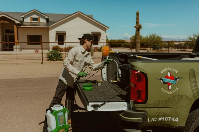NEARPEST team member in a light shirt preparing a backpack sprayer beside the pickup
