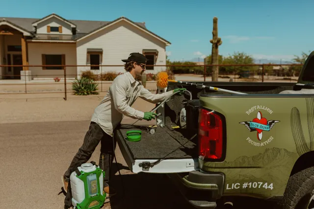 NEARPEST team member in a light shirt preparing a backpack sprayer beside the pickup