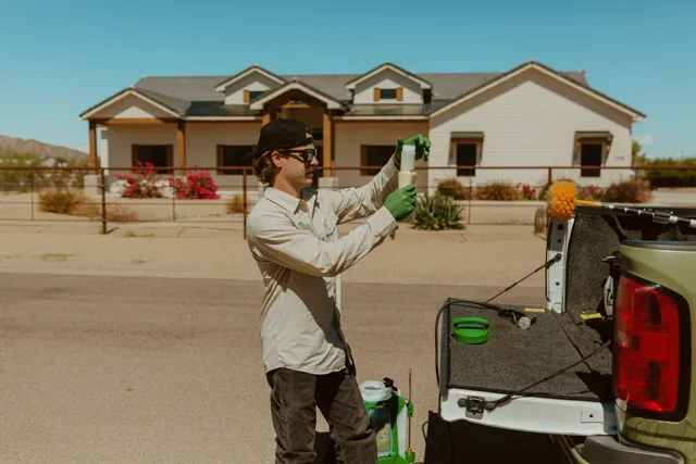NEARPEST team member in a light shirt preparing a backpack sprayer beside the pickup