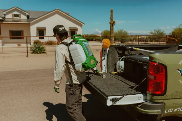 NEARPEST team member in a light shirt preparing a backpack sprayer beside the pickup