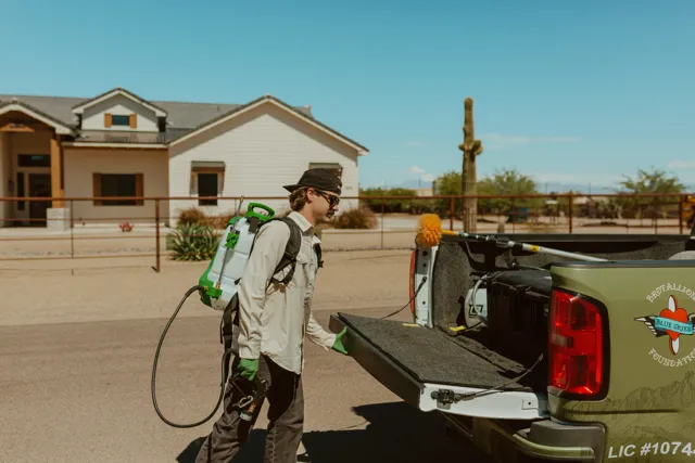 NEARPEST team member in a light shirt preparing a backpack sprayer beside the pickup