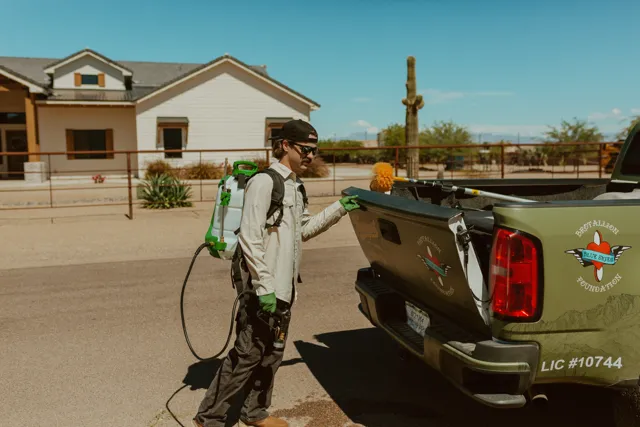 NEARPEST team member in a light shirt preparing a backpack sprayer beside the pickup