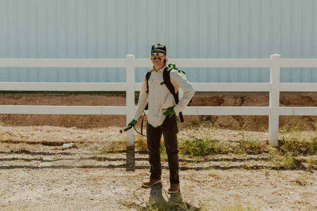 NEARPEST team member wearing a backpack sprayer beside a white rail fence