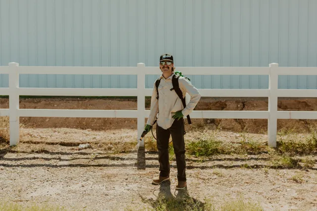 NEARPEST team member wearing a backpack sprayer beside a white rail fence