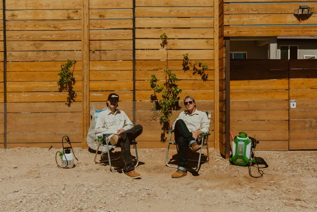 The two NEARPEST owners seated outside a wood-sided building with pest-control equipment