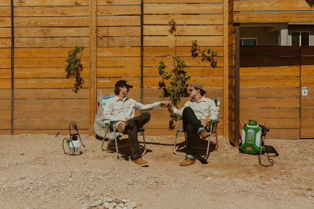 The two NEARPEST owners seated outside a wood-sided building with pest-control equipment