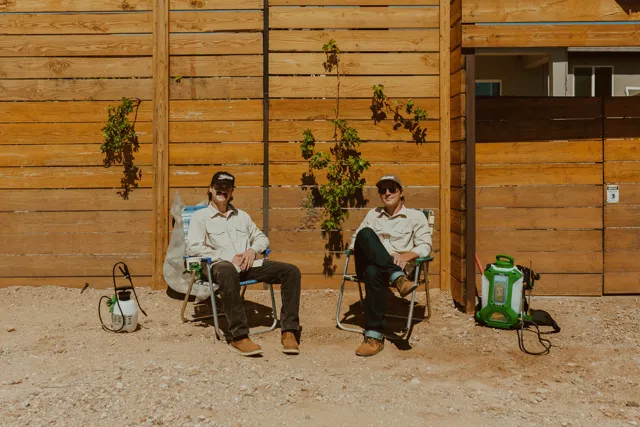 The two NEARPEST owners seated outside a wood-sided building with pest-control equipment