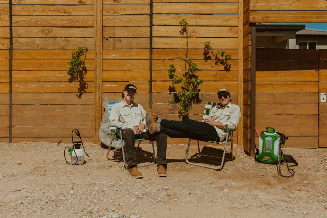 The two NEARPEST owners seated outside a wood-sided building with pest-control equipment