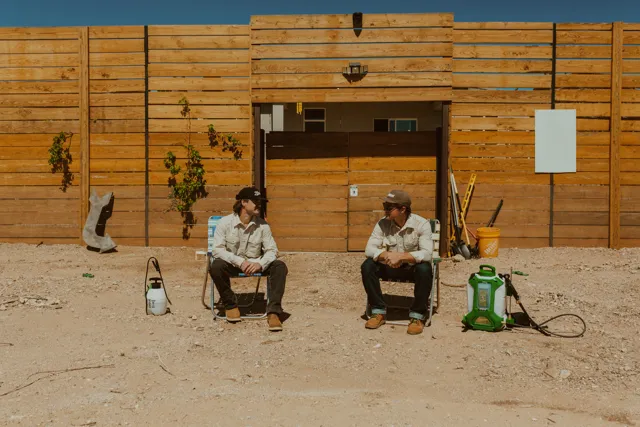 The two NEARPEST owners seated outside a wood-sided building with pest-control equipment