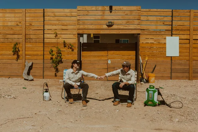 The two NEARPEST owners seated outside a wood-sided building with pest-control equipment