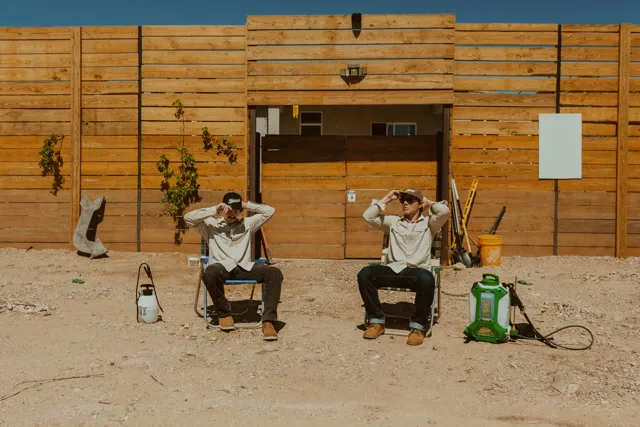 The two NEARPEST owners seated outside a wood-sided building with pest-control equipment