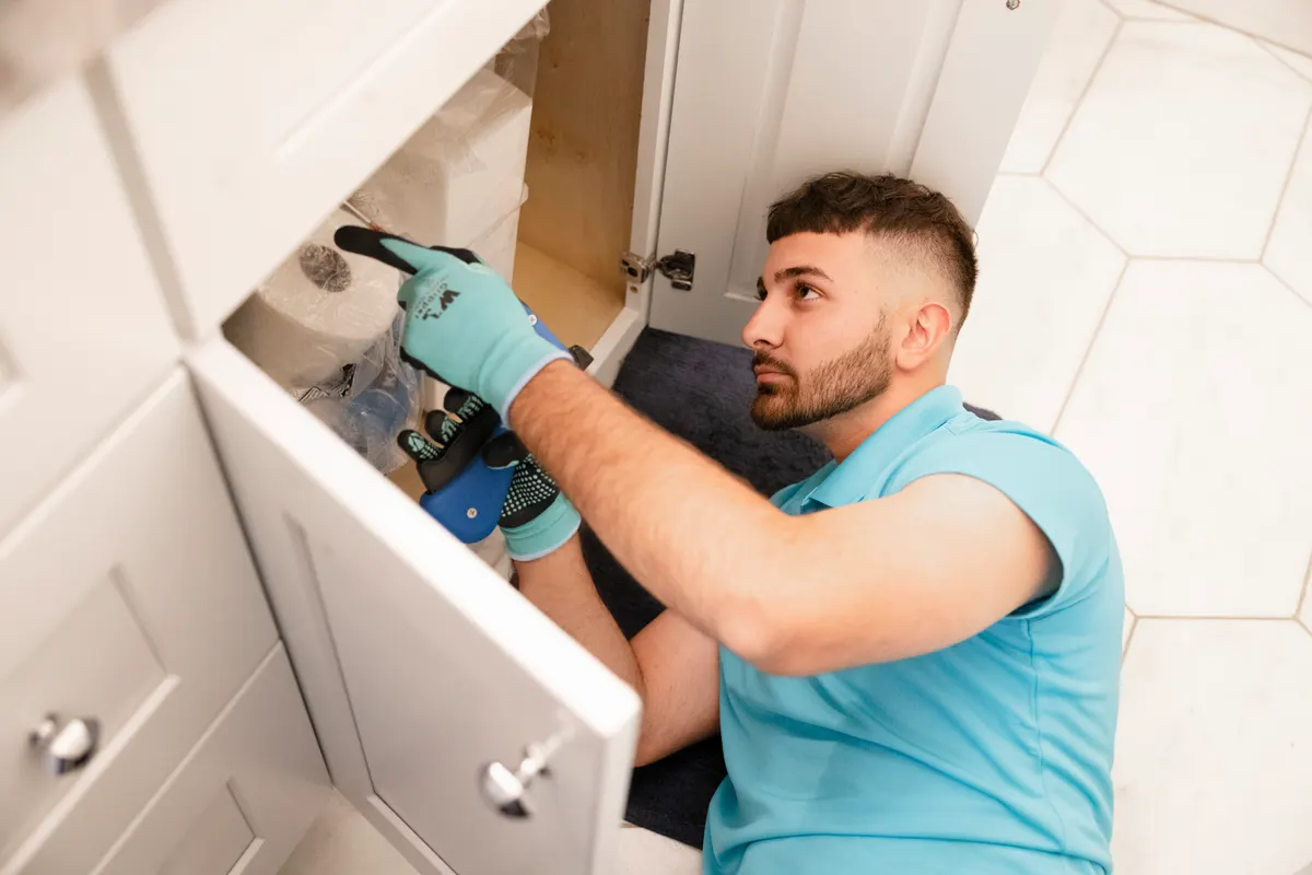 Technician inspecting under a kitchen sink cabinet for moisture and pest activity